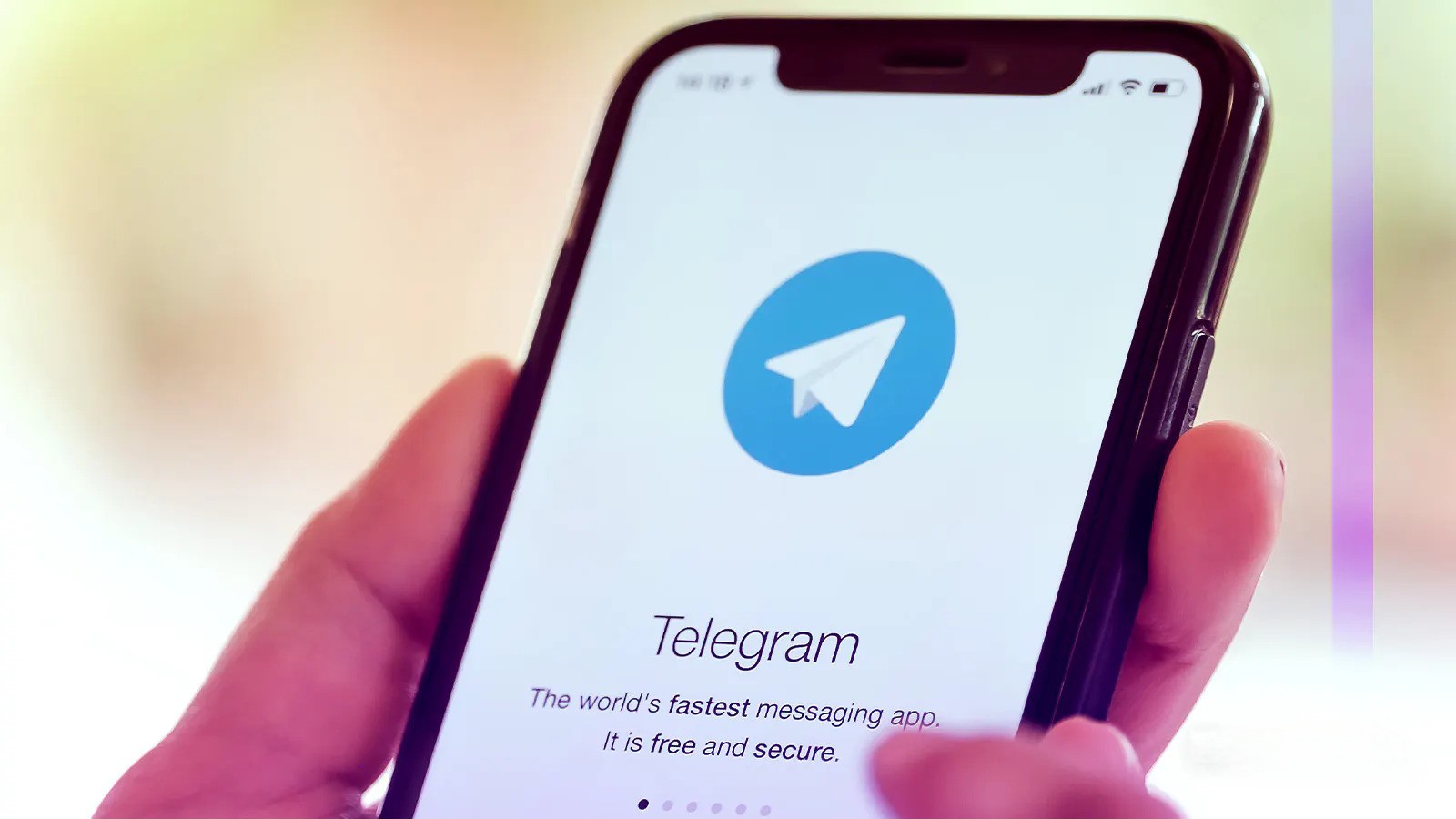 Egy kéz tart egy okostelefont, amelynek képernyőjén a Telegram alkalmazás logója látható. A logó alatt a "Telegram" felirat és a "The world's fastest messaging app. It is free and secure." szöveg olvasható.