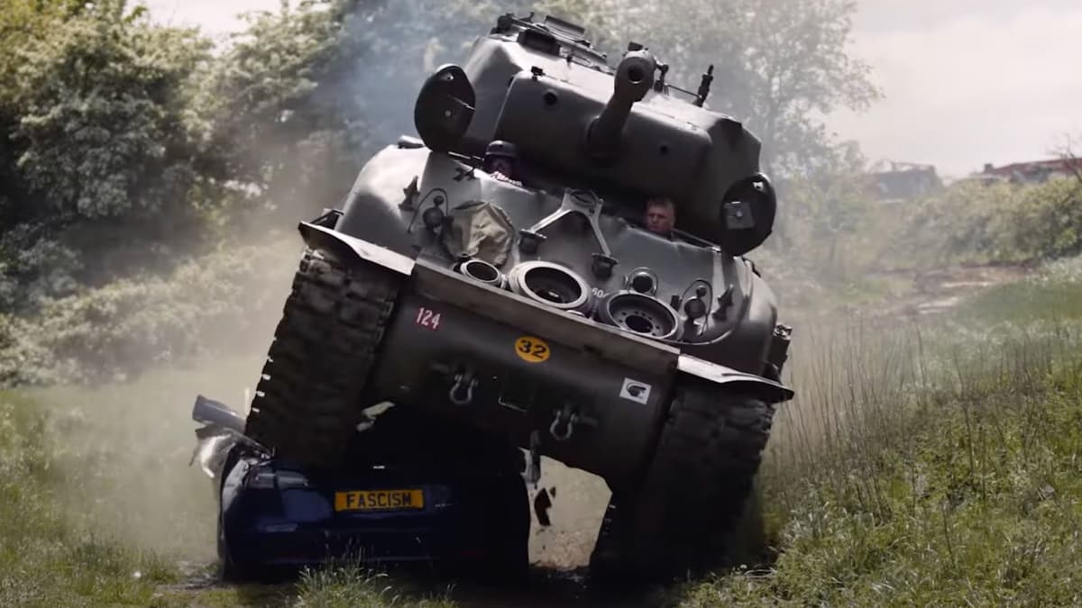 Egy Sherman tank mászik fel egy kék autóra egy füves, fás területen, harctéri környezetben. A tankon "124" és "32" számok láthatók, az autón pedig egy "FASCISM" feliratú rendszámtábla. A háttérben füst és köd, valamint fák és bokrok láthatóak, ami háborús hangulatot idéz. A tank tornyában egy katona áll, sisakban.